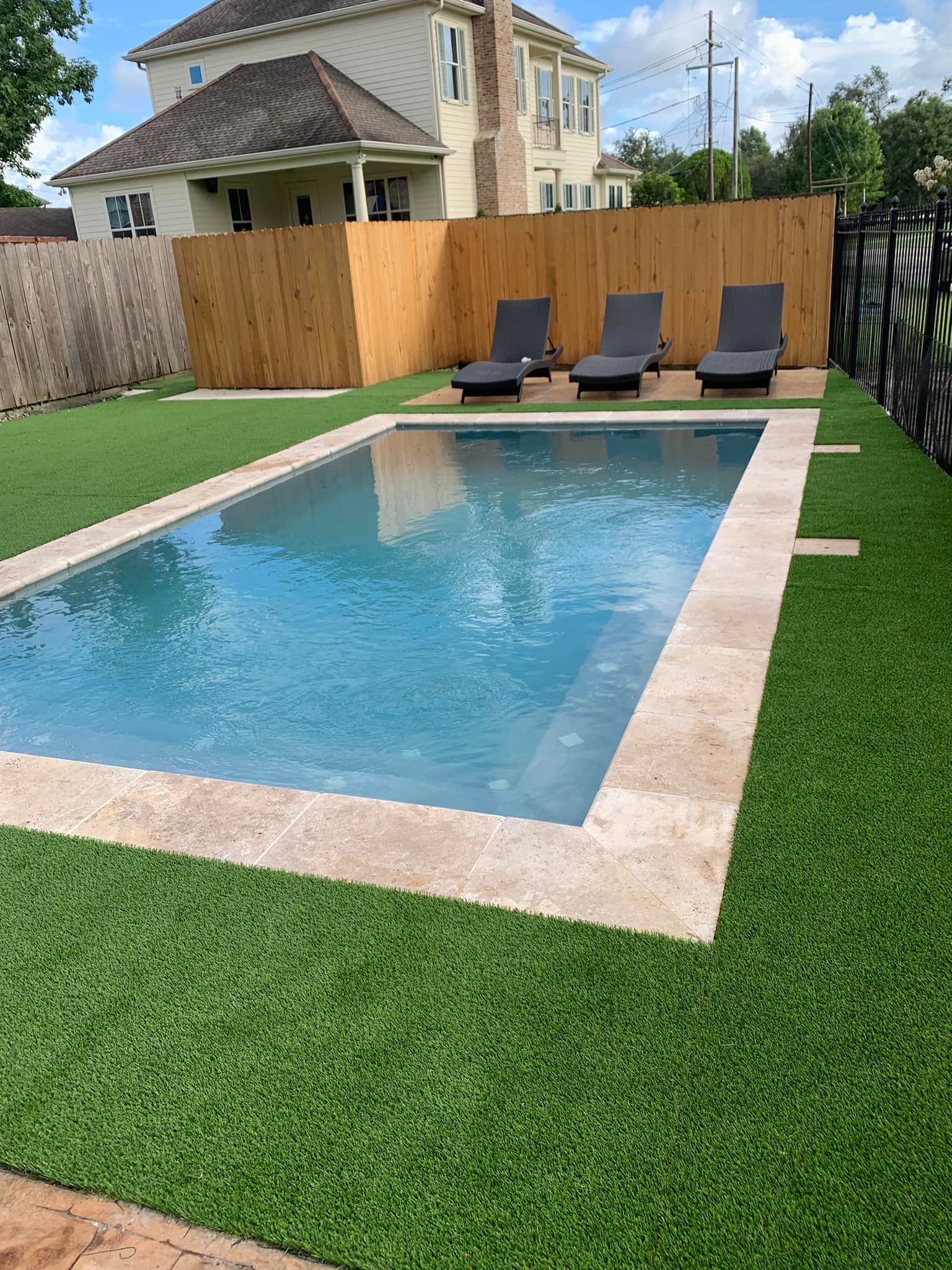 A large swimming pool surrounded by lawn chairs and a wooden fence.