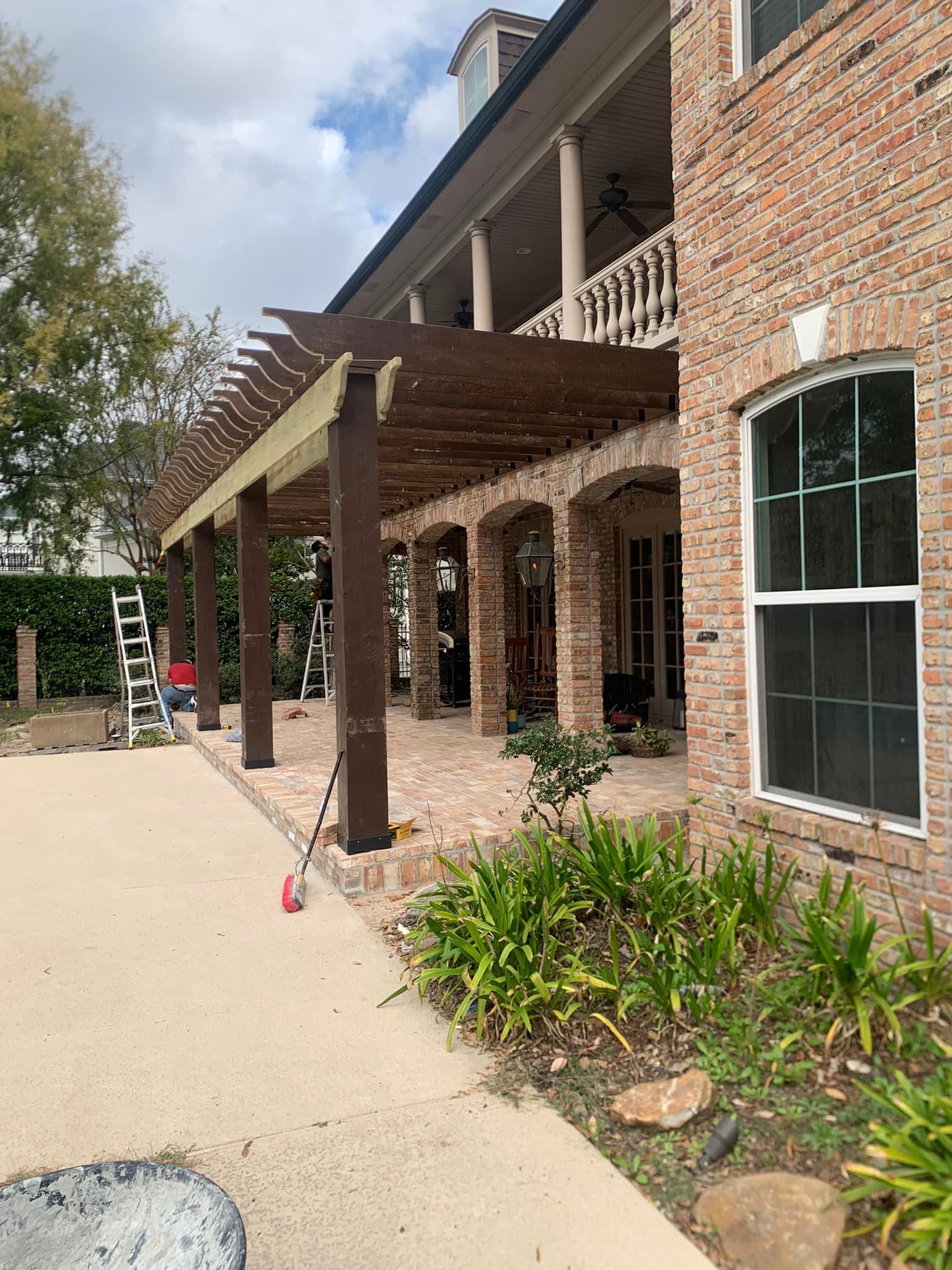 A large brick house with a pergola and a ladder in front of it.
