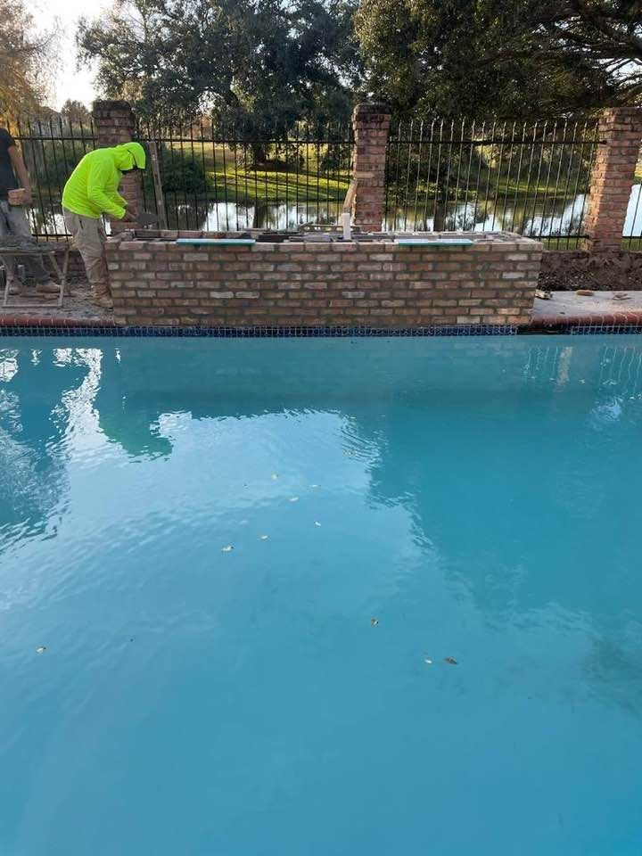 A man is working on a brick wall next to a swimming pool.