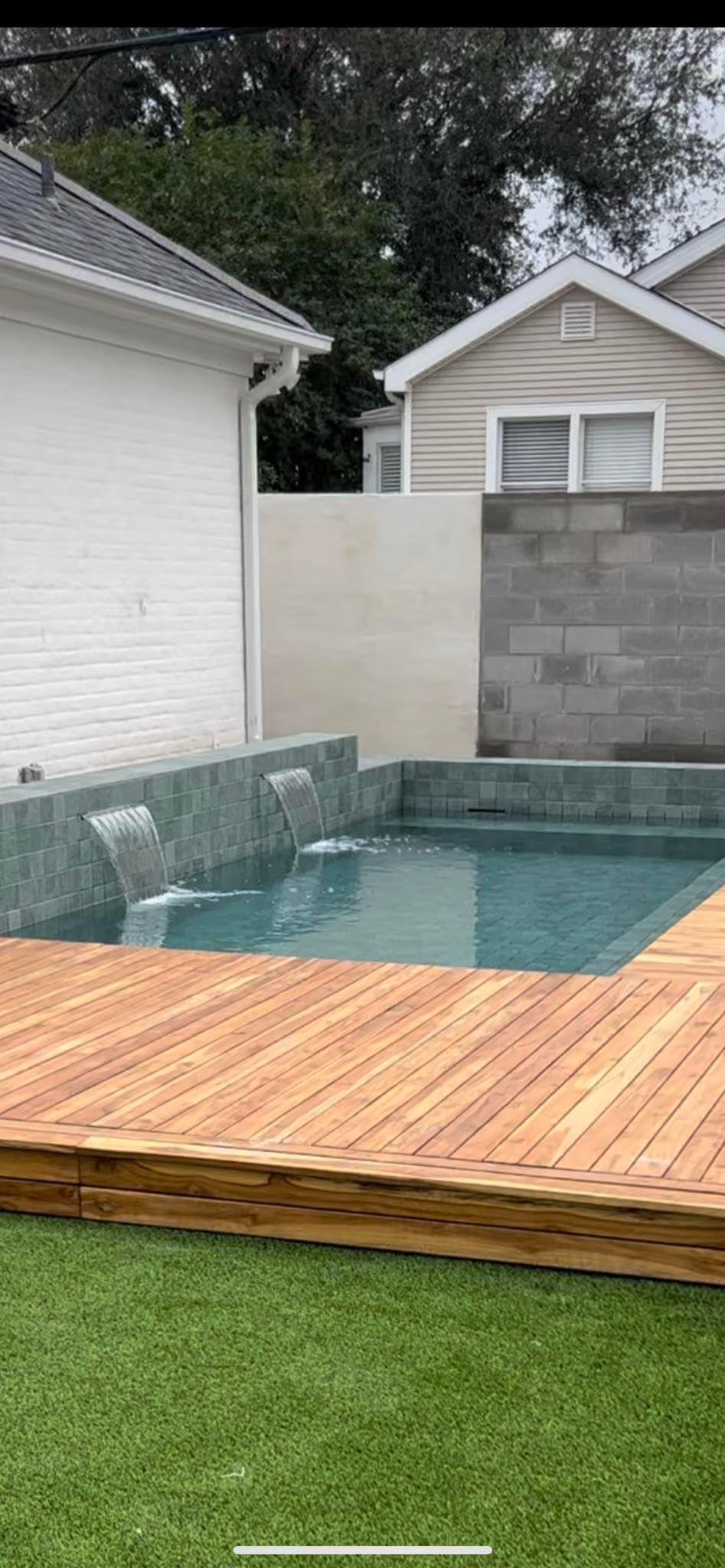 A swimming pool with a wooden deck in front of a house.