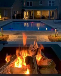 A fire pit is lit up in front of a swimming pool.