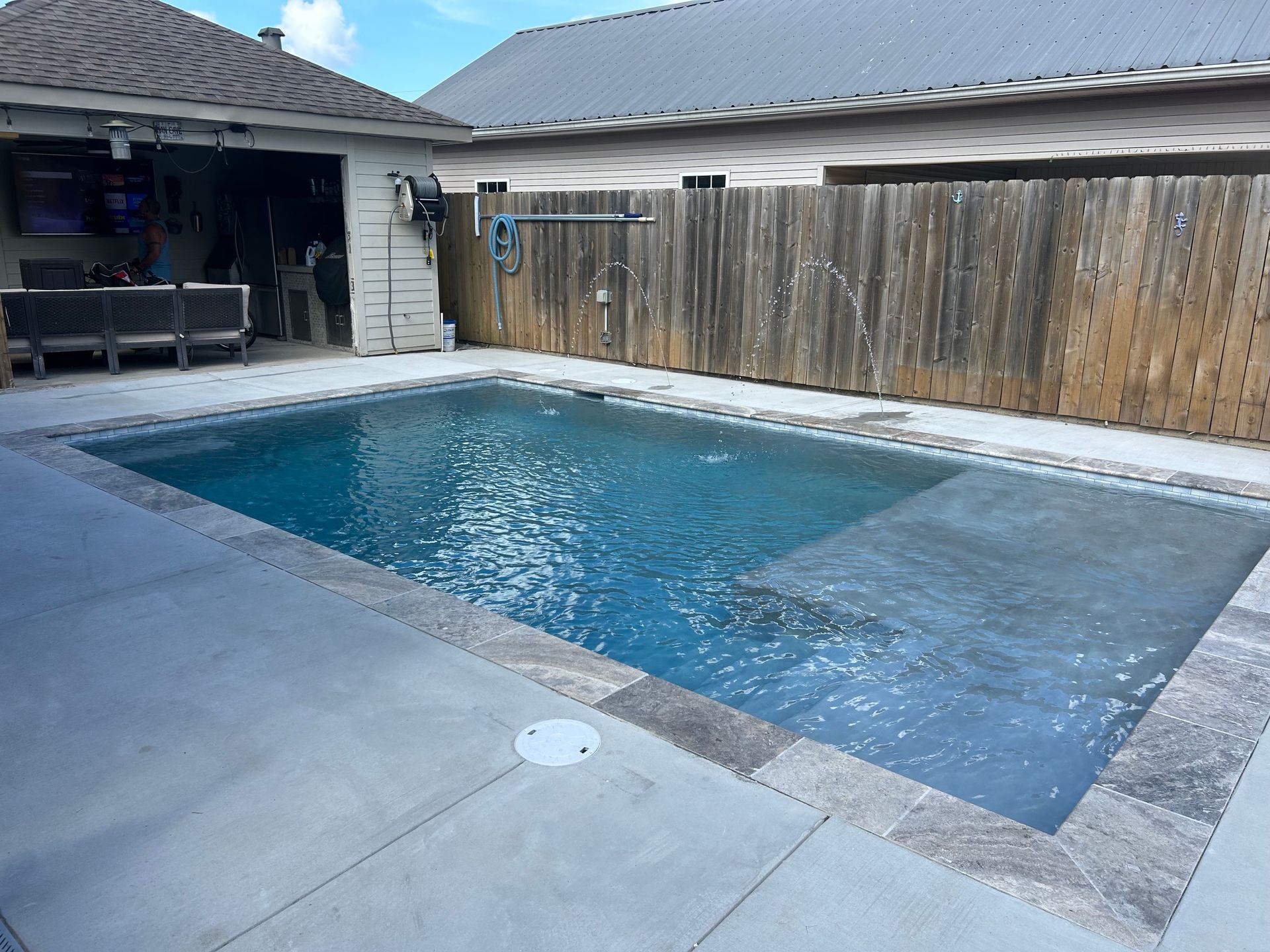 Backyard swimming pool with blue water, concrete patio, and wooden privacy fence.