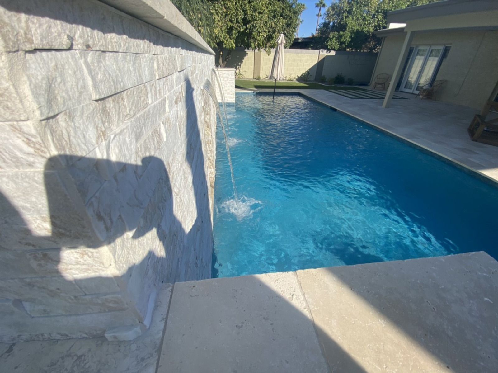 A large swimming pool with a waterfall in the backyard of a house.