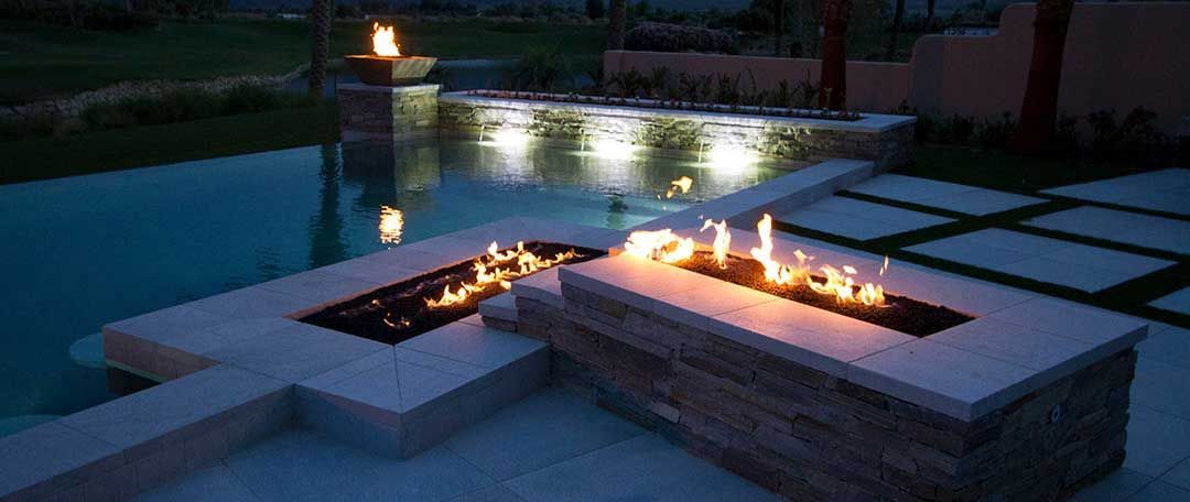 A fire pit is lit up in front of a swimming pool at night.