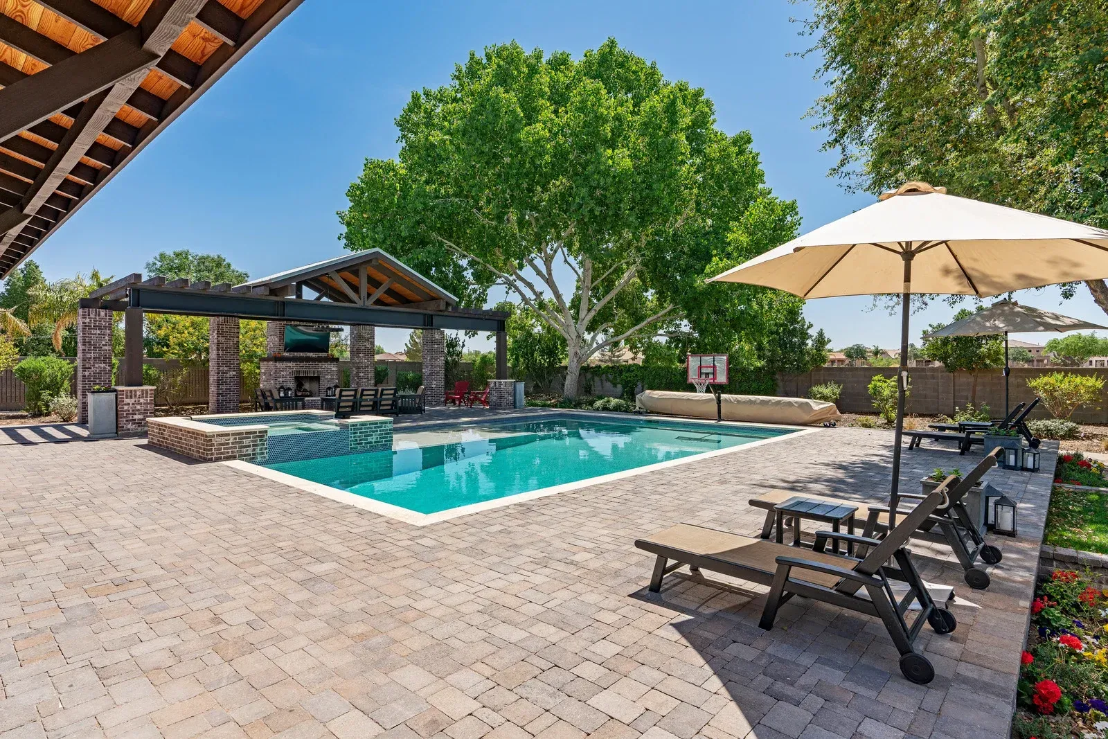 A large swimming pool is surrounded by chairs and umbrellas in a backyard.