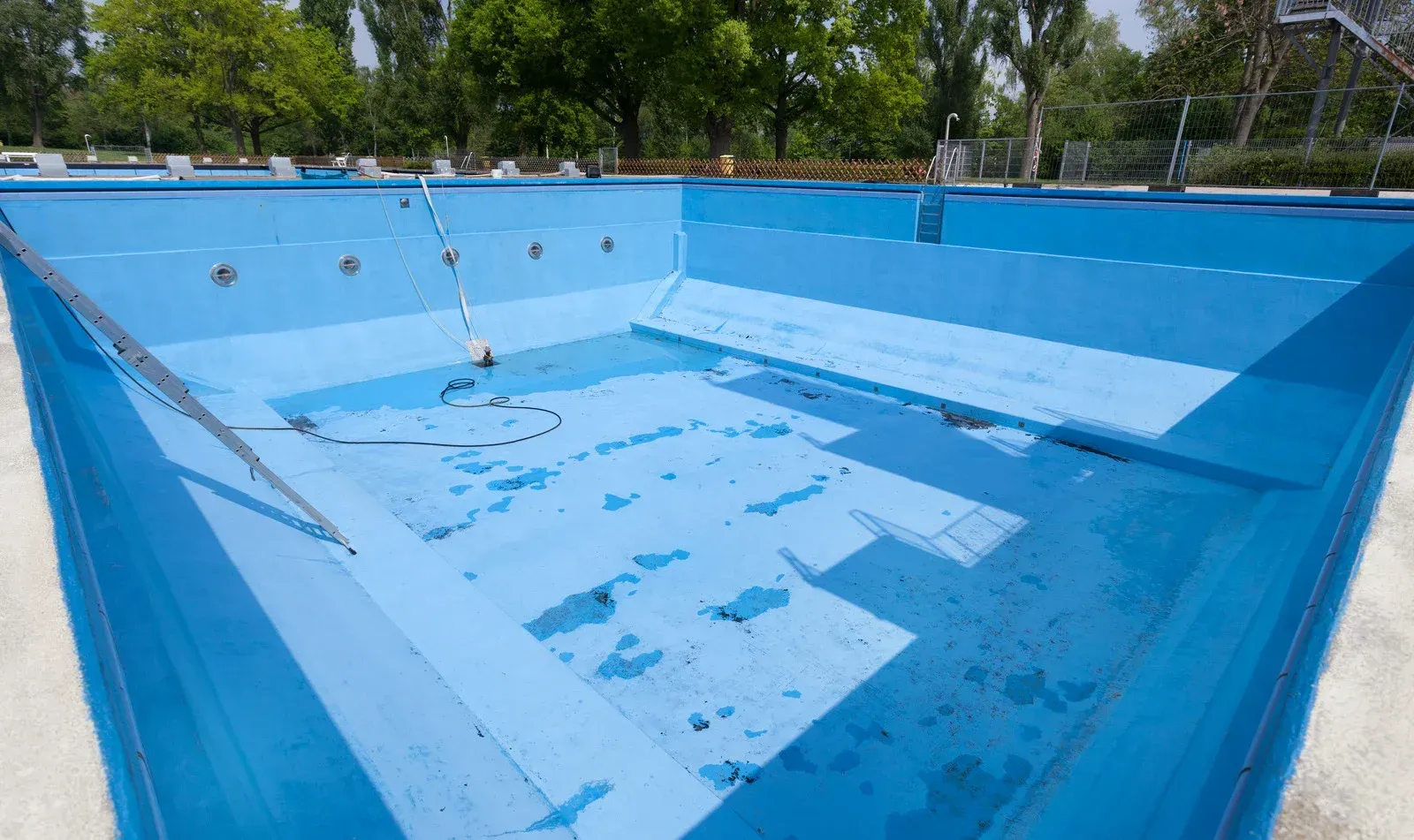 An empty swimming pool with blue water and trees in the background.