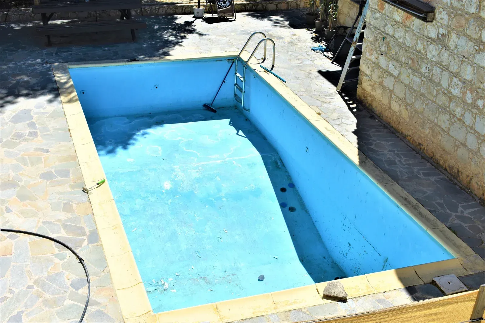 An empty swimming pool is sitting on top of a stone patio.