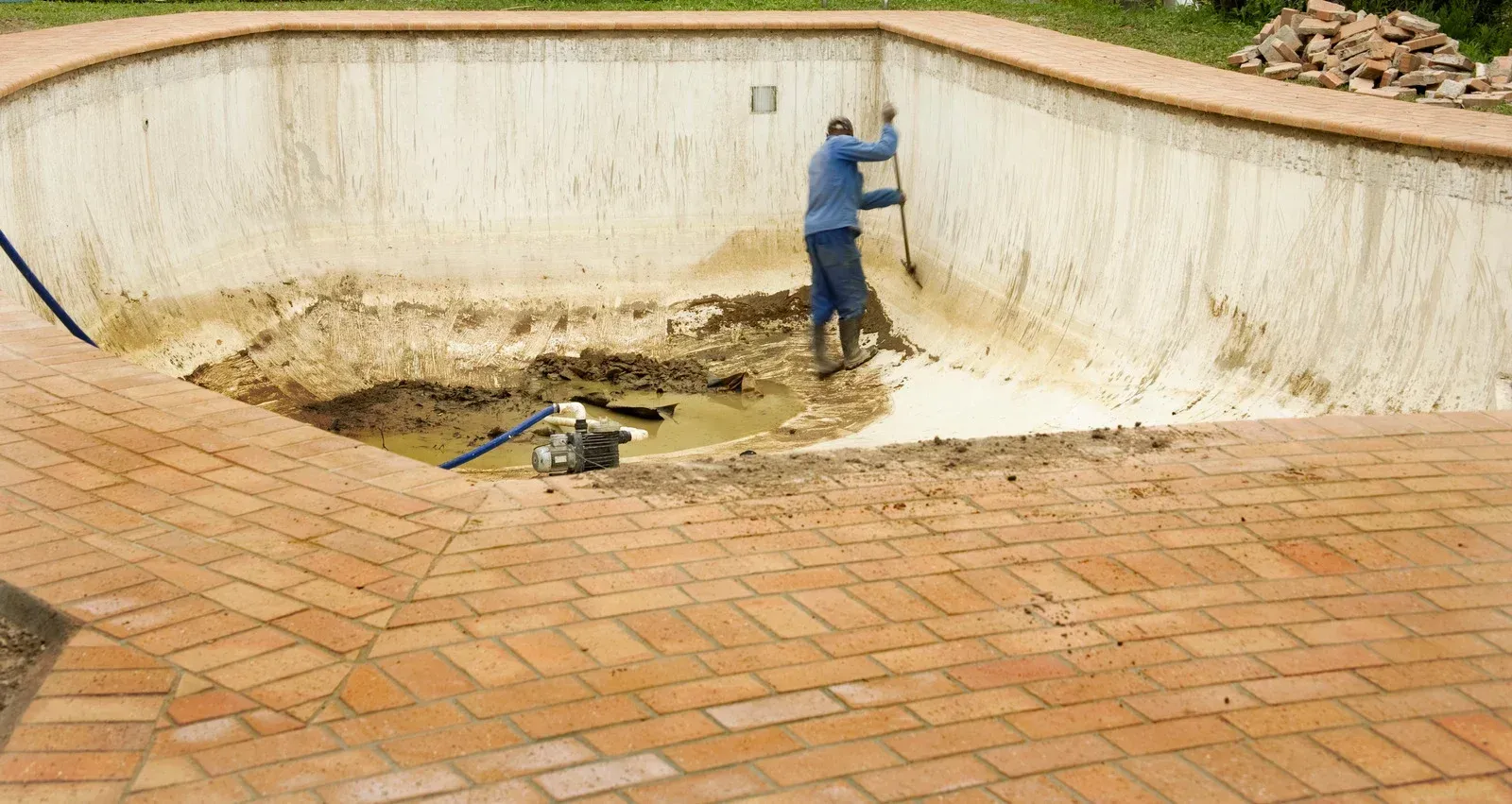 A man is digging a hole in the side of a swimming pool.