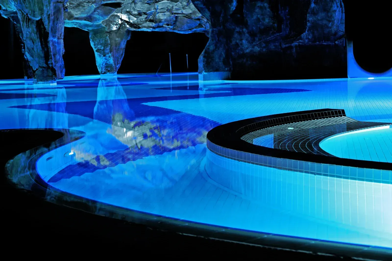 A swimming pool is lit up with blue lights at night.