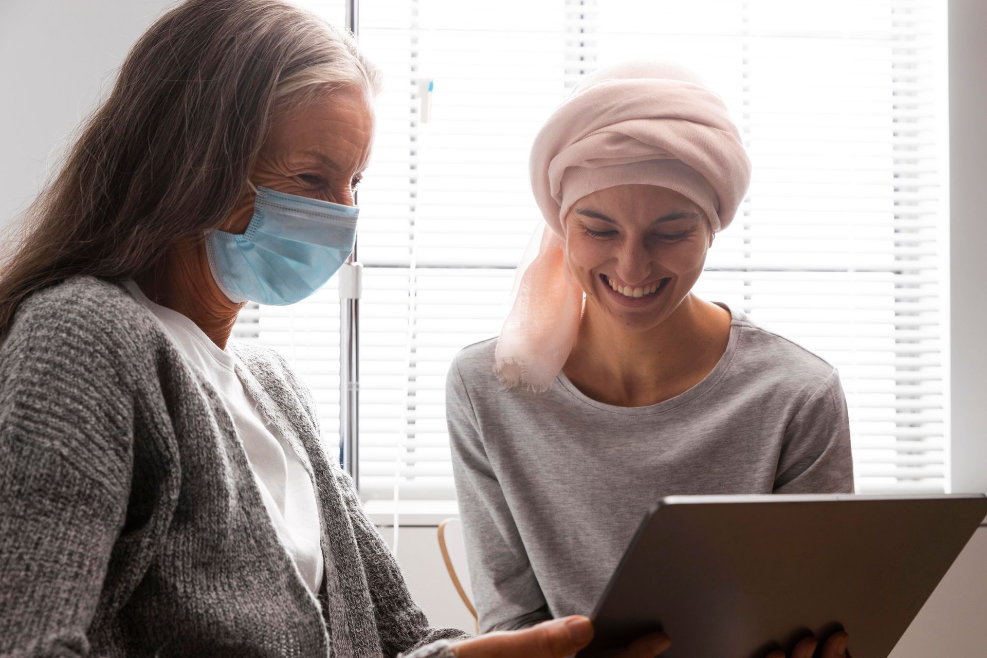 A woman wearing a mask is looking at a tablet with another woman.