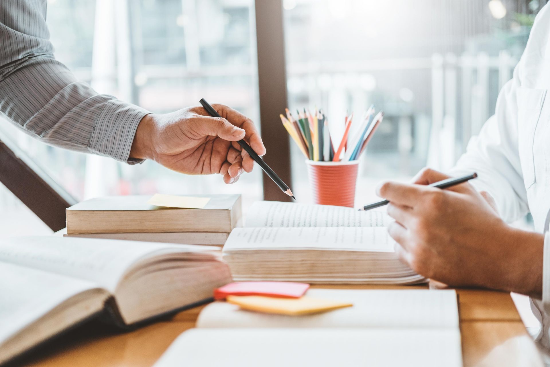 Two people studying books together, one pointing with a pen.