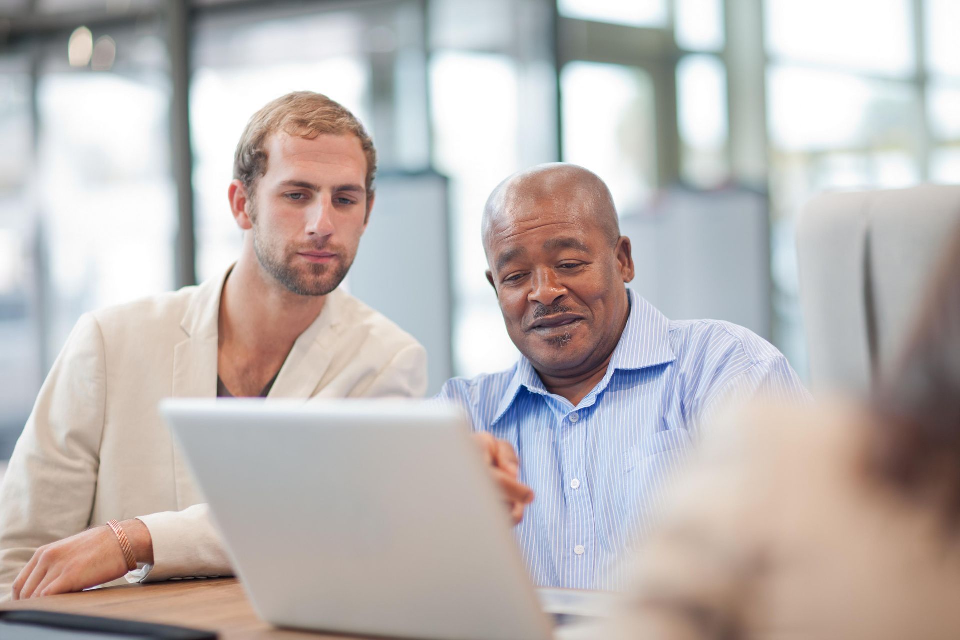 Two men look at a laptop screen together, one points.