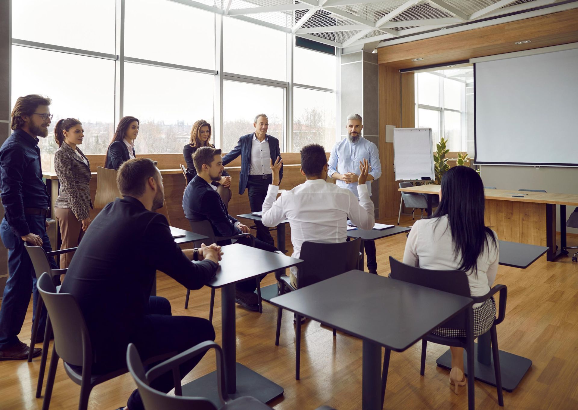 Business presentation in a modern office. People are attending a meeting, some seated, some standing.
