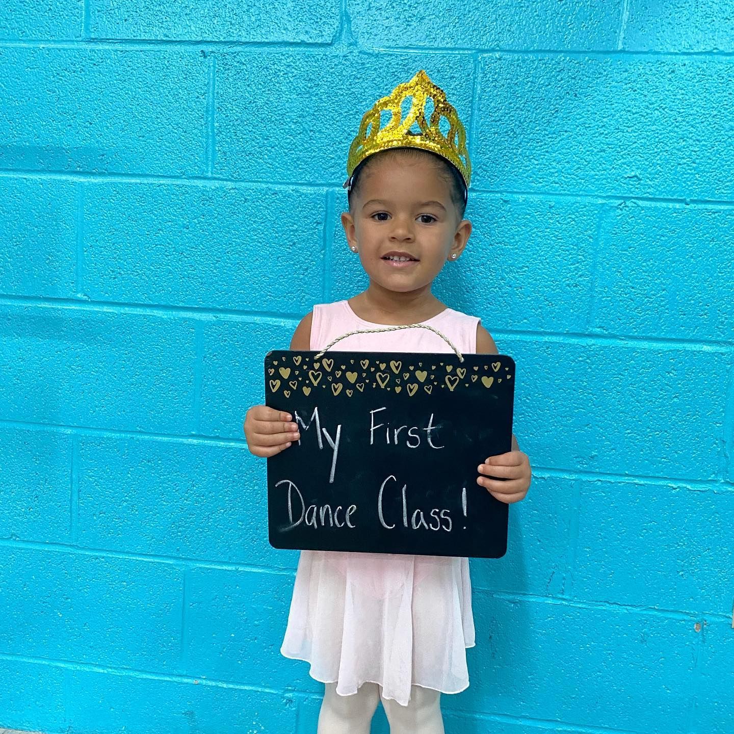 A little girl is holding a sign that says my first dance class