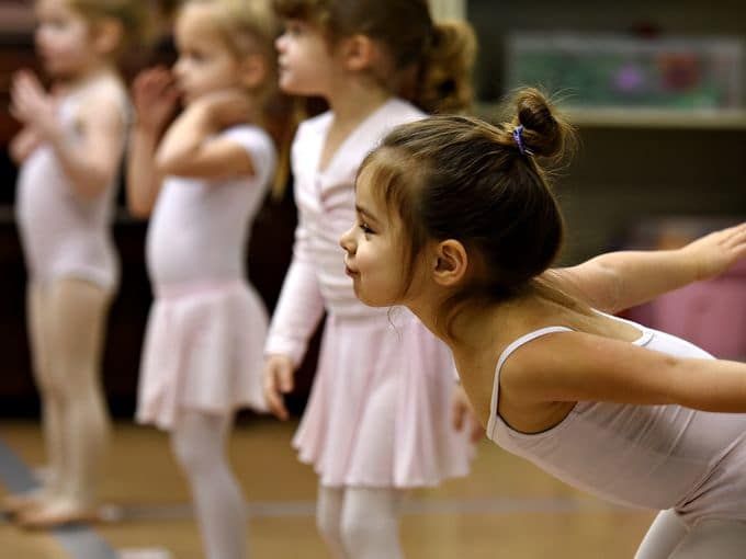 Three little dancers are sitting next to each waiting for ballet class.