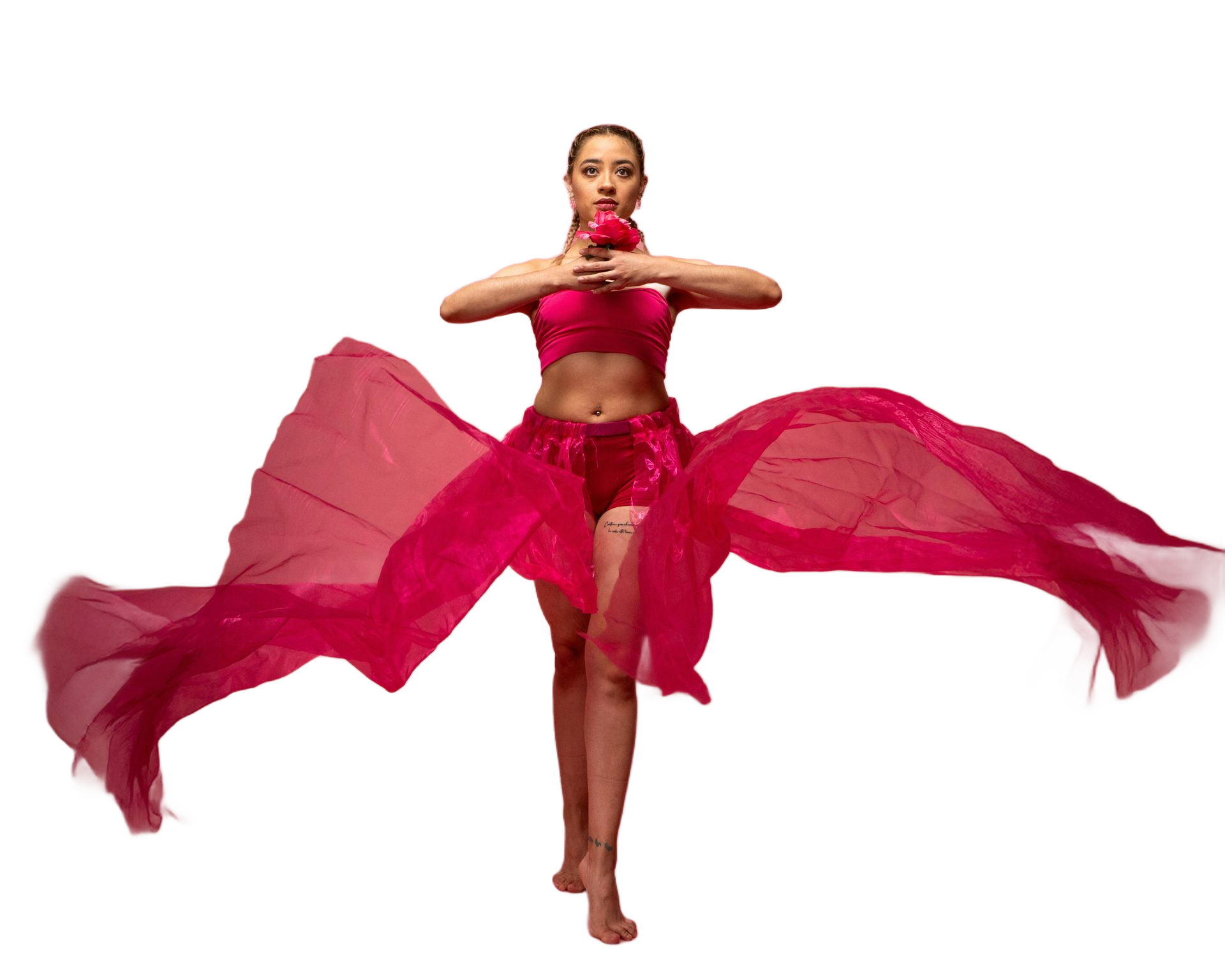 Woman in pink crop top and skirt, arms raised holding an object, with flowing fabric against a pink backdrop.