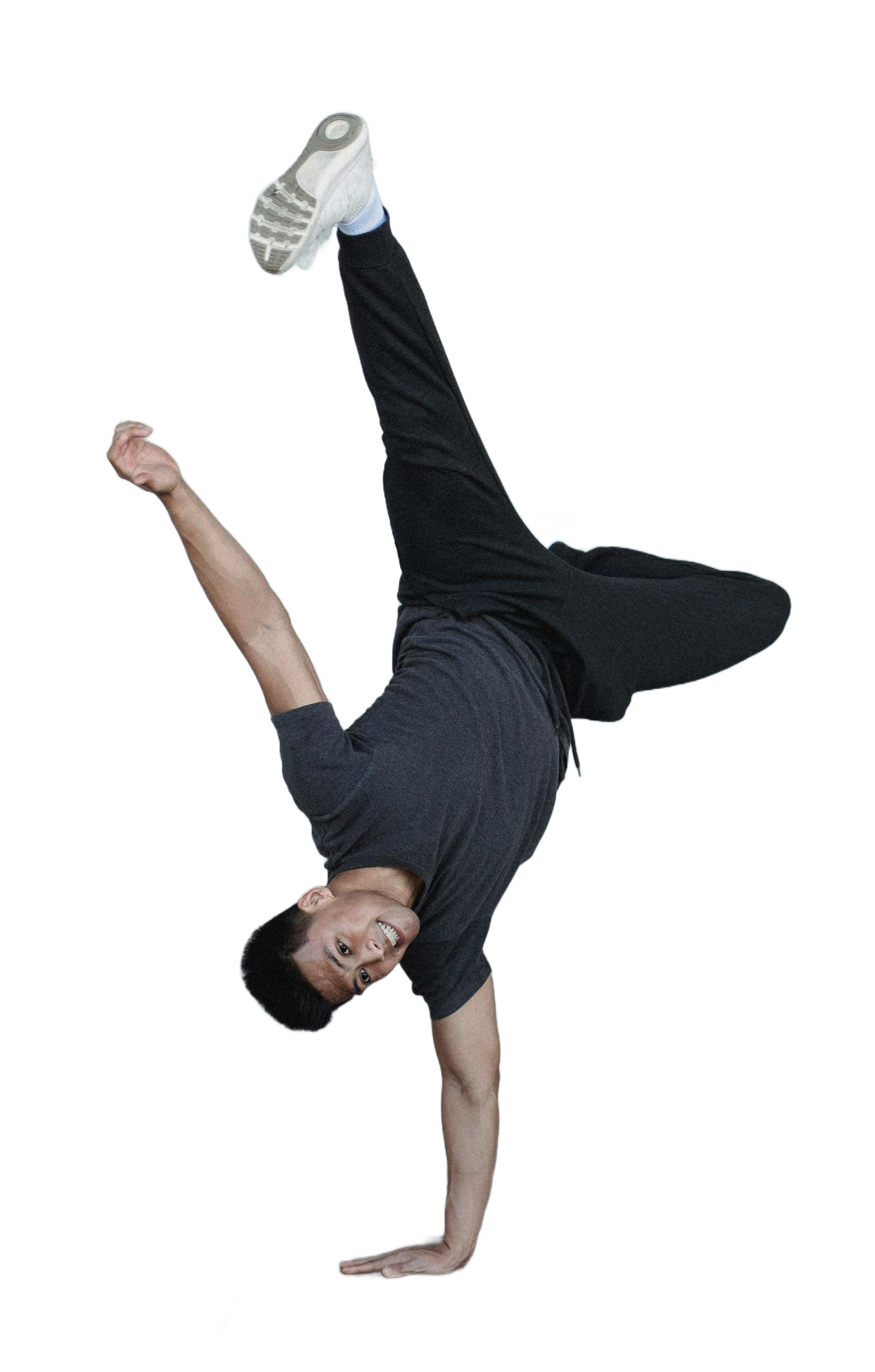 A young man breakdancing on one hand against a gray concrete wall. He wears black pants and a gray shirt, with one leg raised.