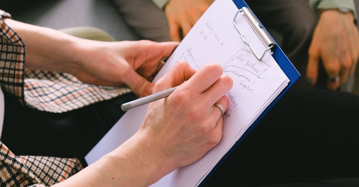 A person holds a blue clipboard and uses a pen to take handwritten notes on a white sheet of paper.