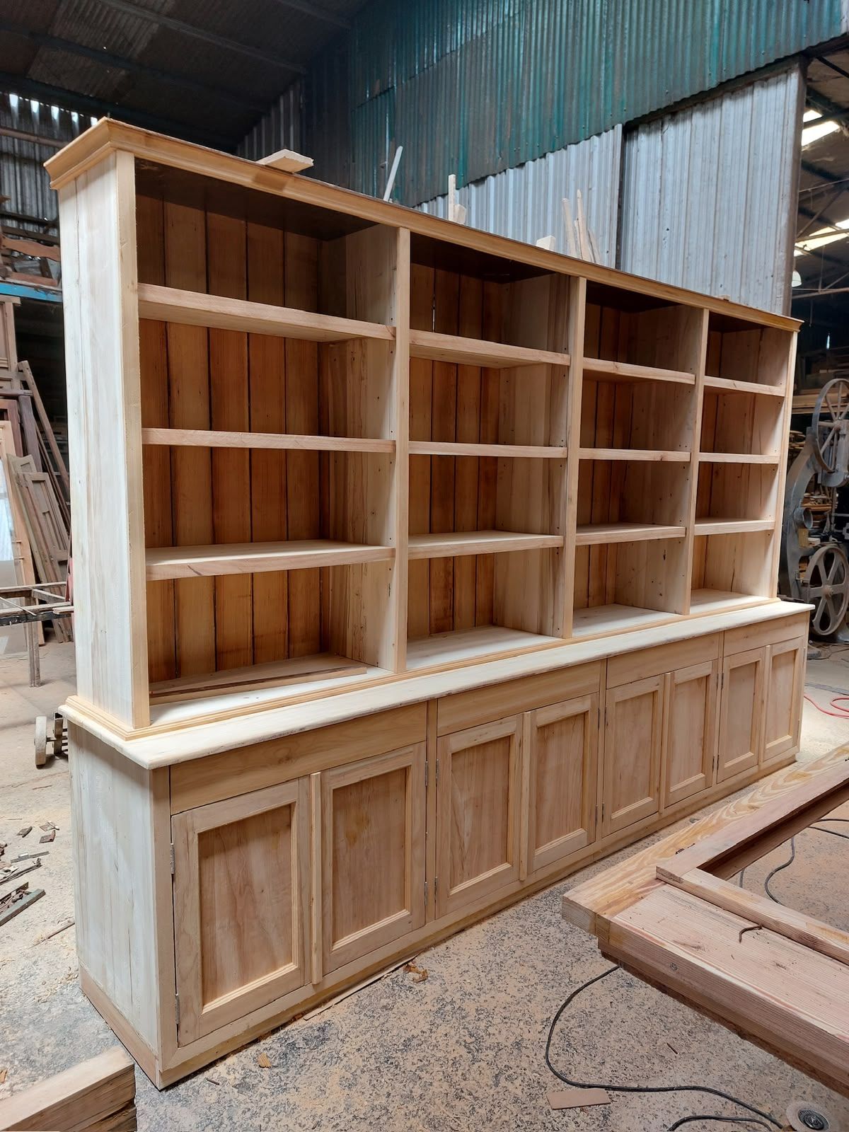 Amplio armario de madera sin acabado con estantes y base panelada en un entorno de taller.