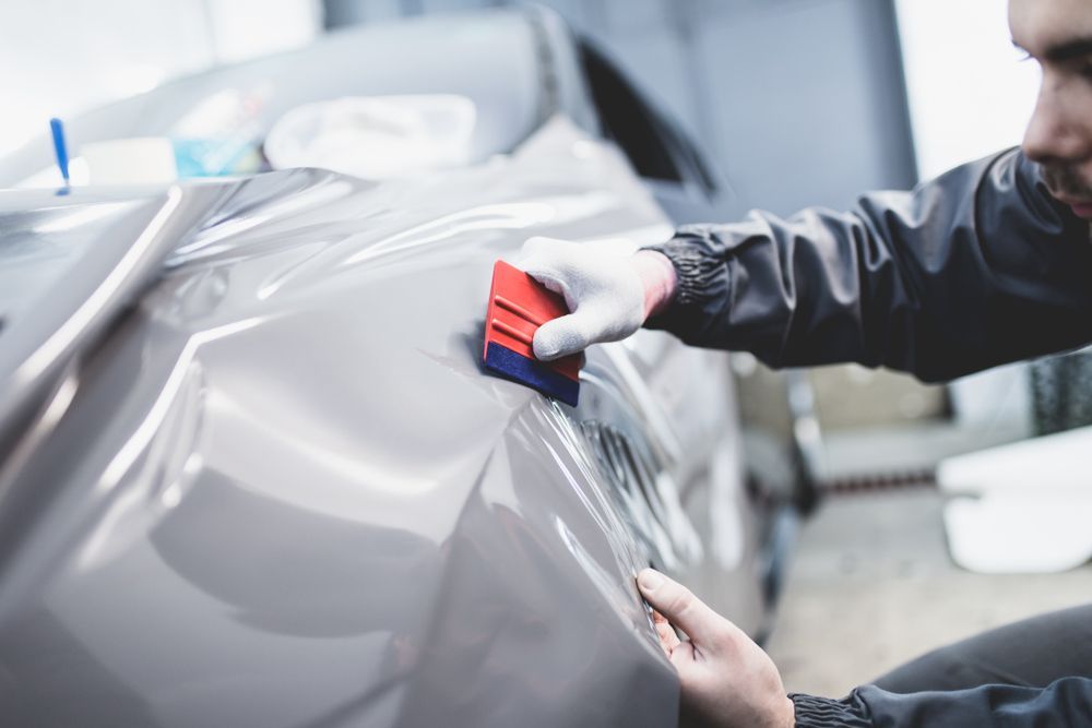 Person Applying Grey Vinyl Wrap to a Car's Side — TrueGloss Elite Coatings In Central Coast, NSW