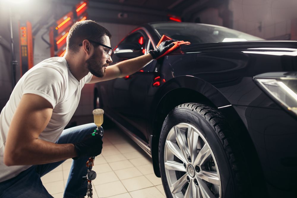 Man in Garage, Polishing a Black Car With Spray Bottle — TrueGloss Elite Coatings In Newcastle, NSW