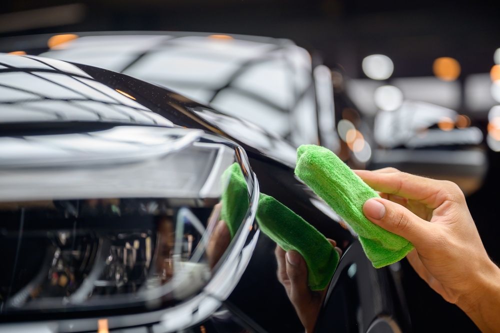 A person uses a green cloth to wipe and polish the glossy black hood of a car — TrueGloss Elite Coatings In Wyong, NSW