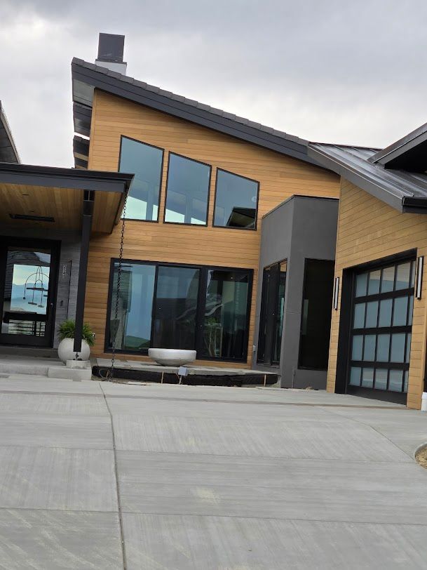 Modern house exterior with wood siding, large windows, and a paved driveway.