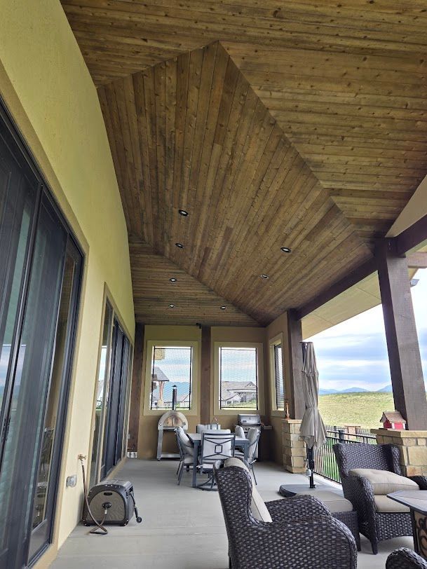 Covered patio with wood ceiling, wicker chairs, and a small table overlooking a scenic lake view