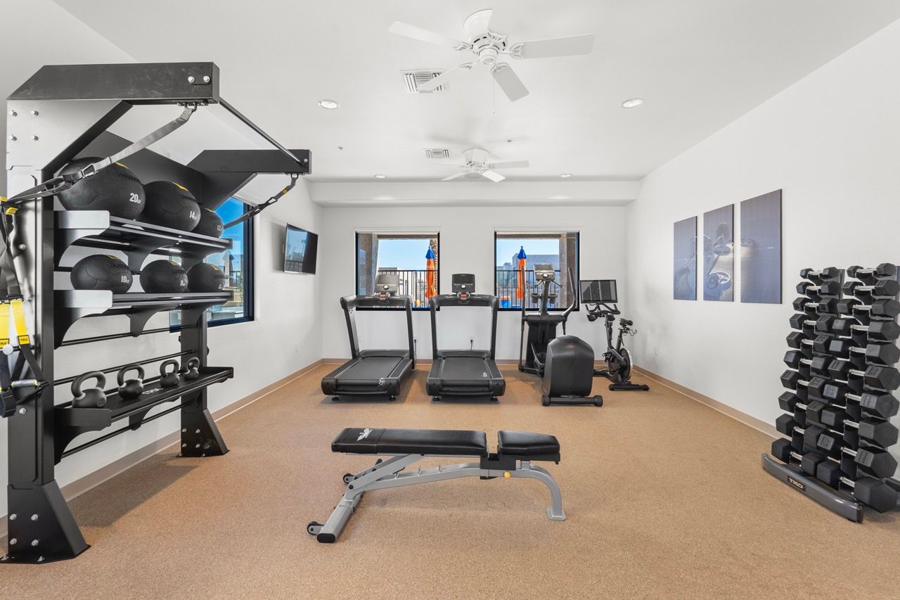 Well-equipped indoor gym in an apartment community with treadmills, weights, and a bench.