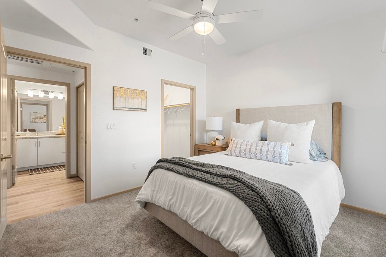 Bedroom in an apartment with a large bed, white linens, beige headboard, and open closet.