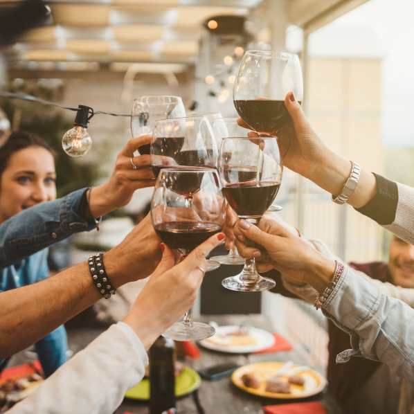 Friends toasting with glasses of red wine at an outdoor table with string lights.