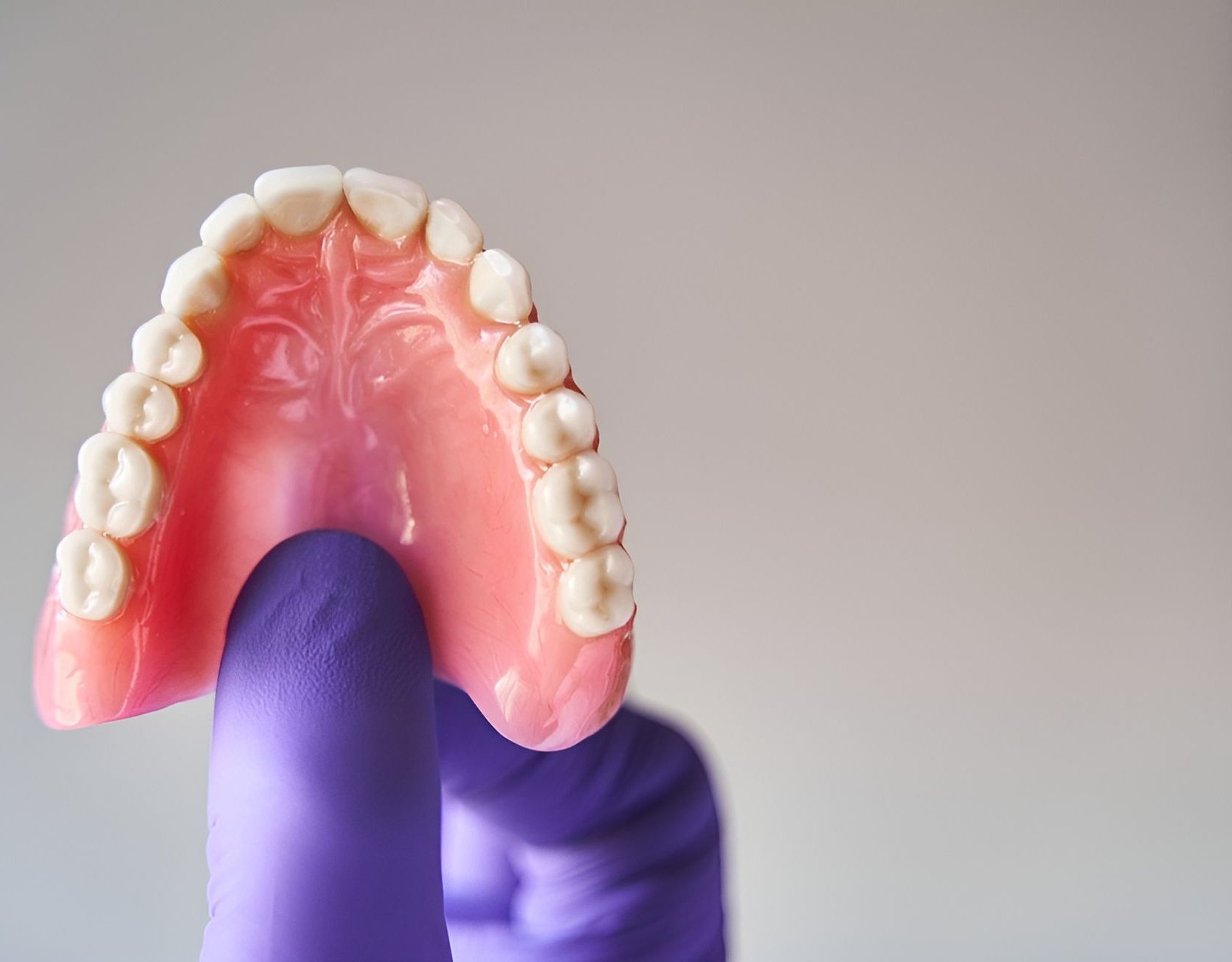 A Person Wearing Purple Gloves is Holding a Denture — Tweed Banora Dental In Tweed Heads South, NSW