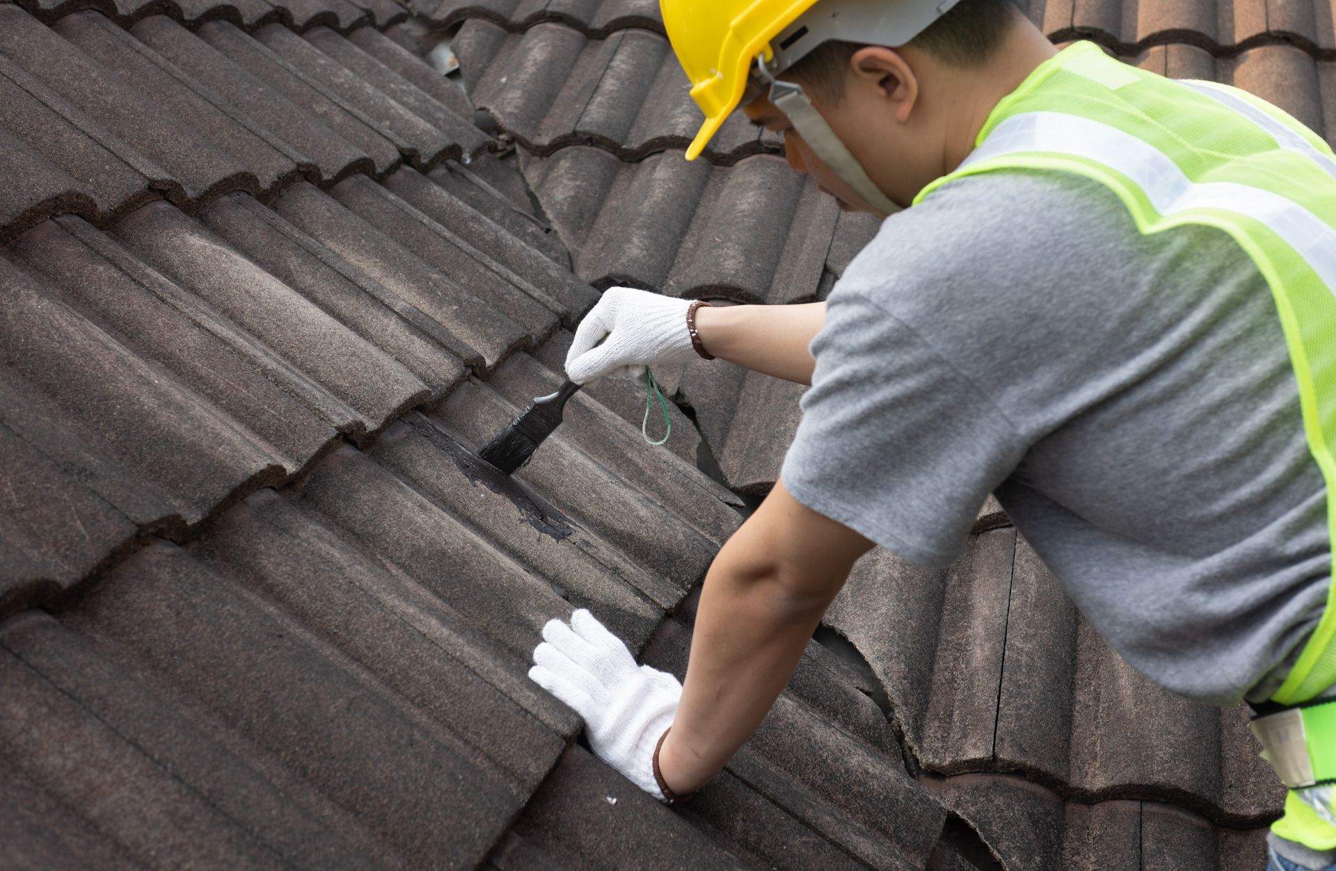 A man wearing a hard hat and safety vest is working on a roof.