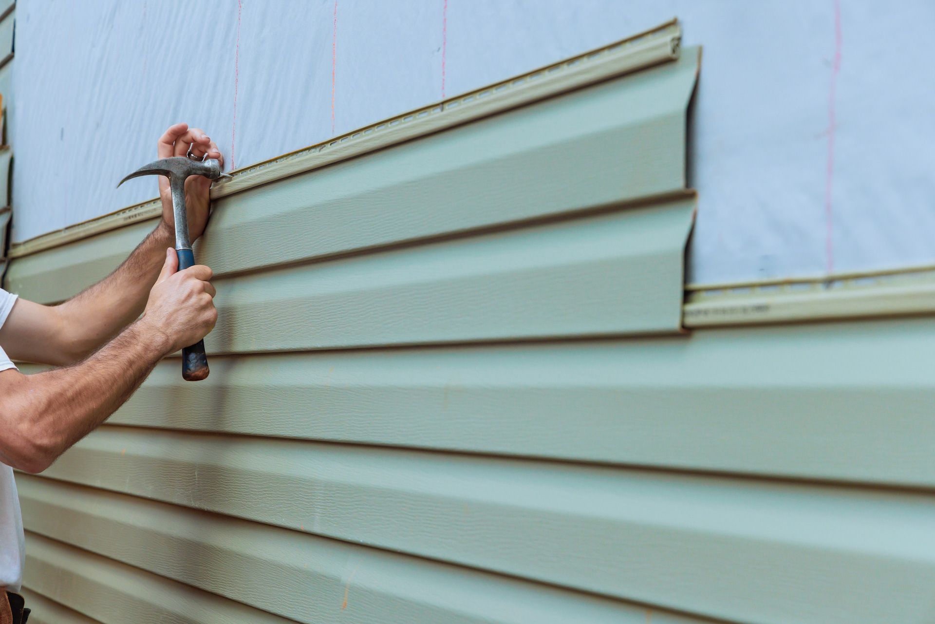 A man is installing siding on a house with a hammer.