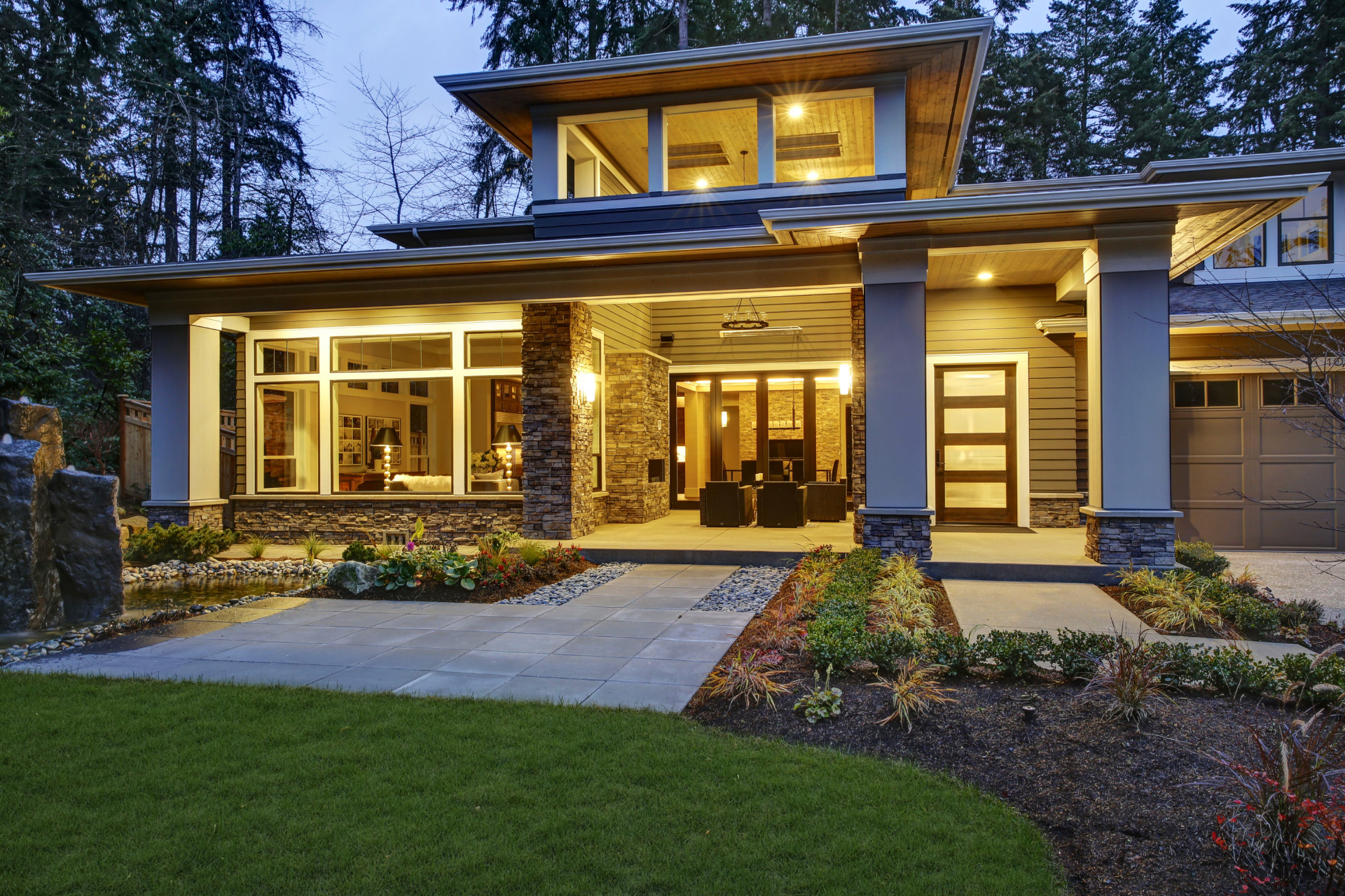Modern two-story house at dusk with warm porch lights, large windows, and a landscaped front yard