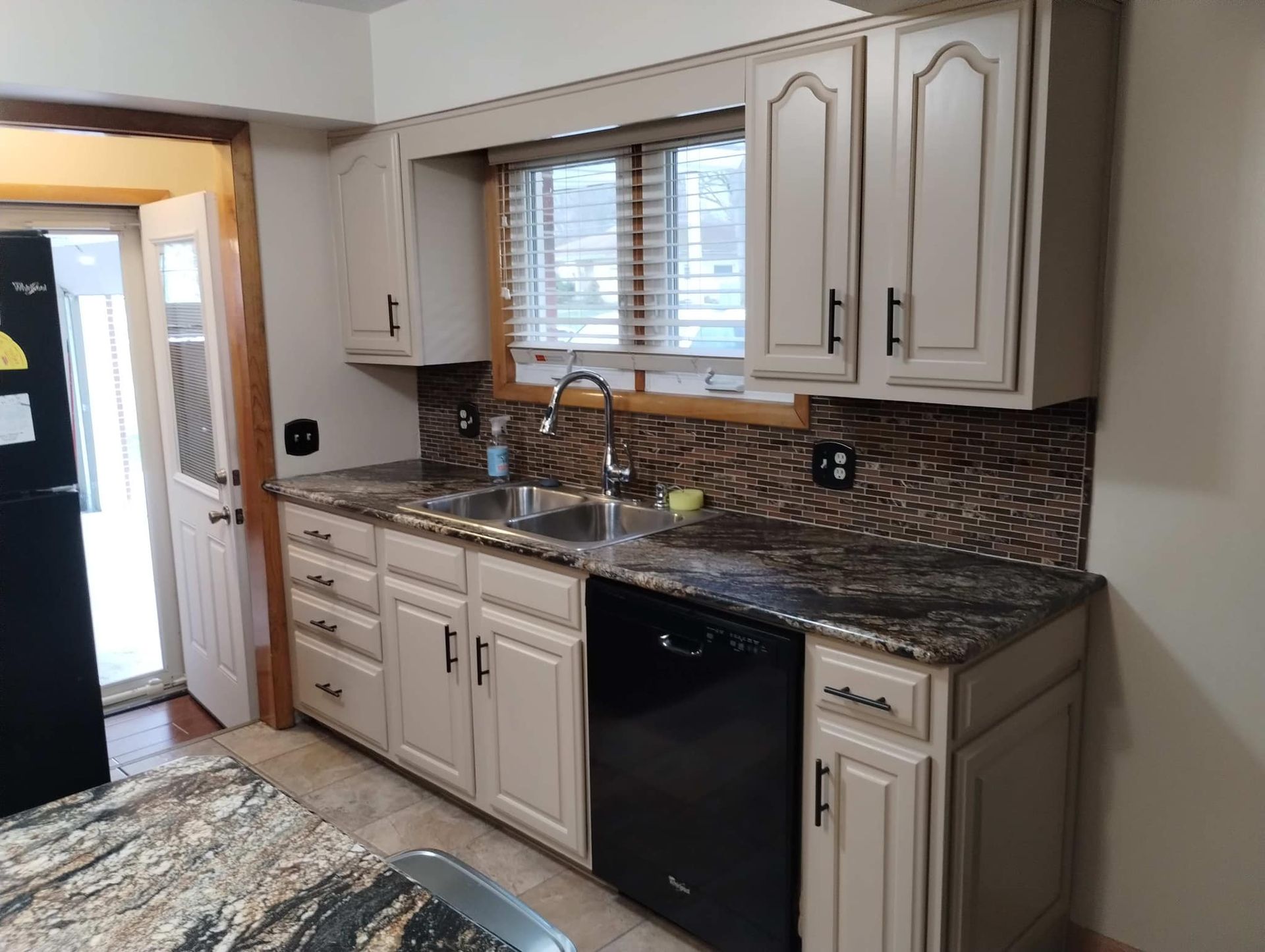 A kitchen with white cabinets , granite counter tops , a sink and a dishwasher.