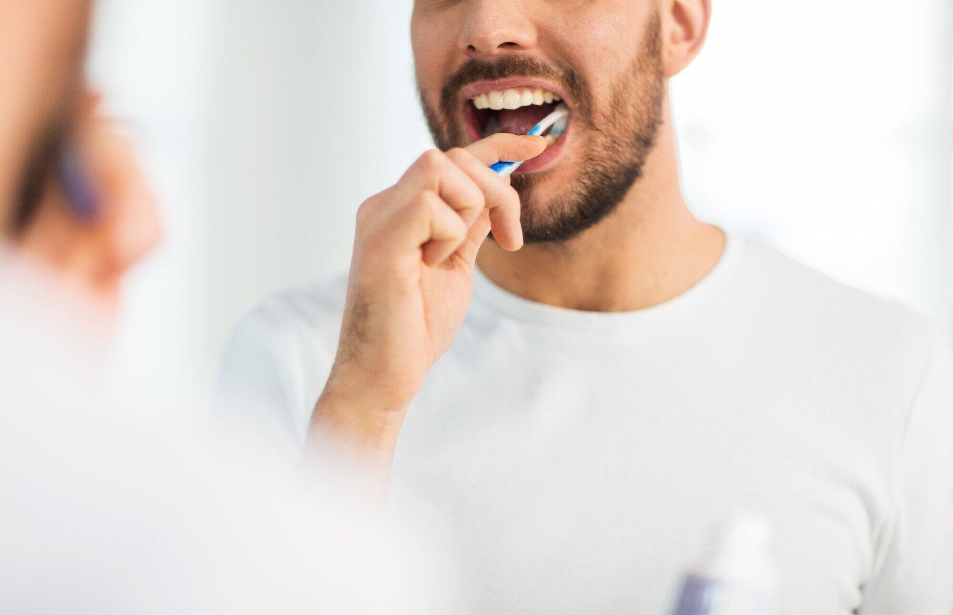 A man is brushing his teeth in front of a mirror.