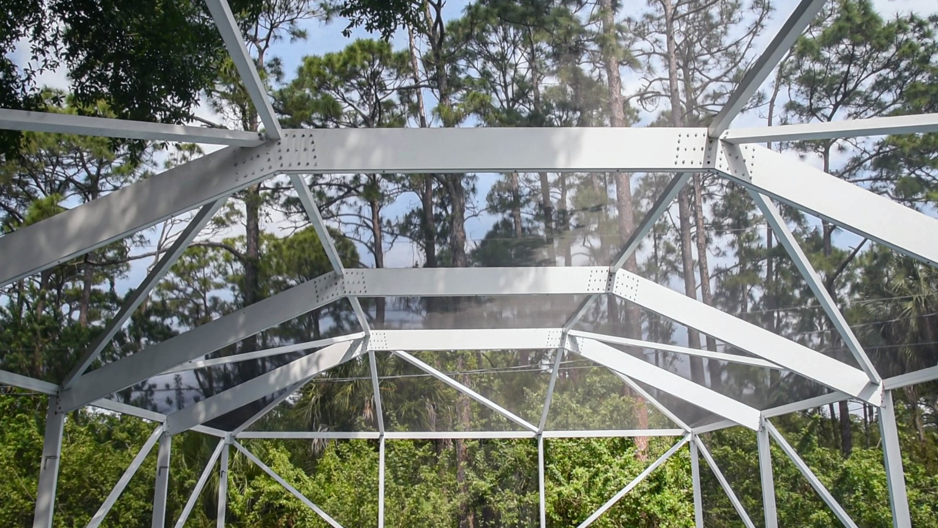 A metal structure with a clear roof is surrounded by trees.