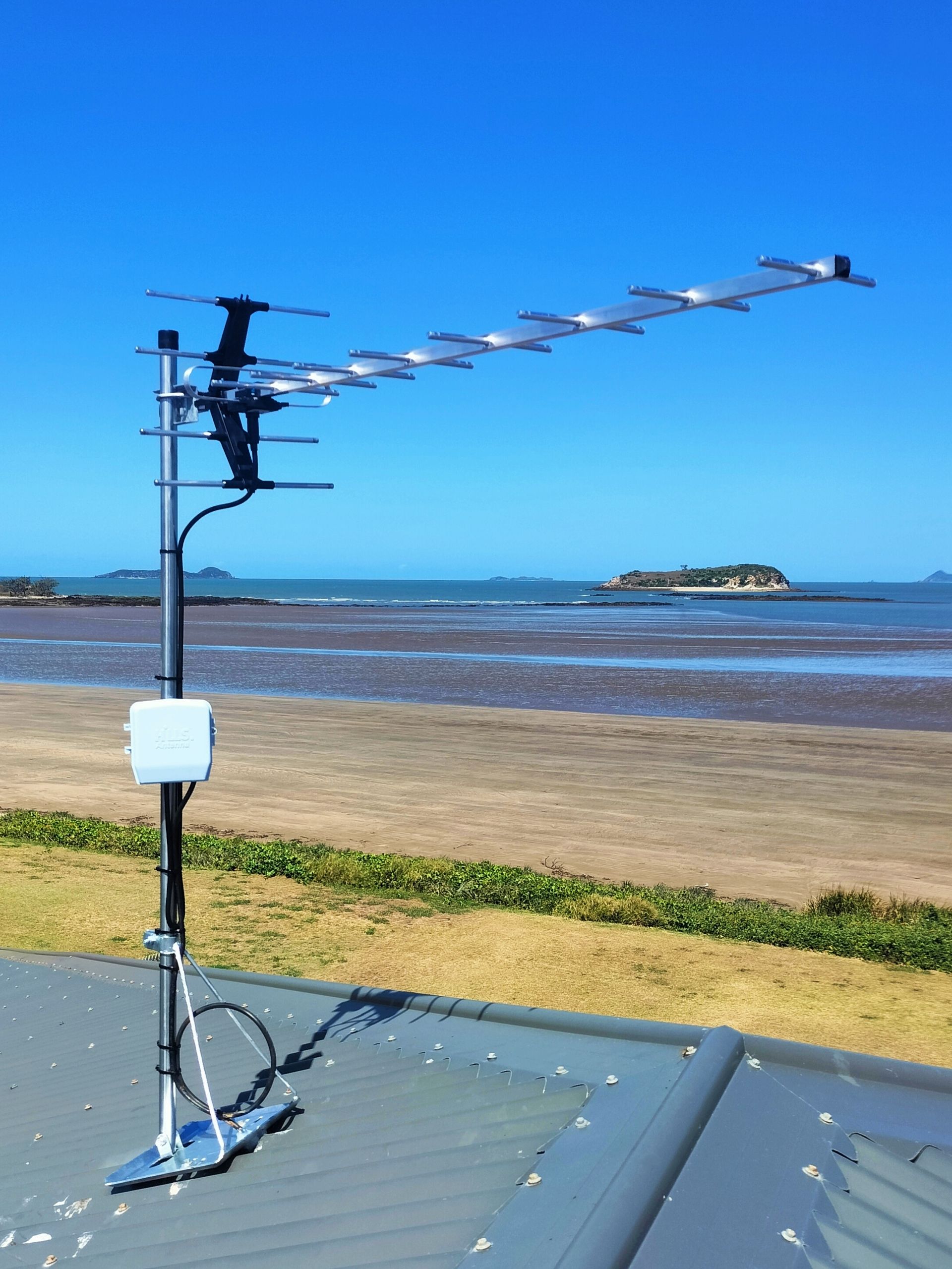 Television antenna on a pole overlooking a beach and ocean under a blue sky.