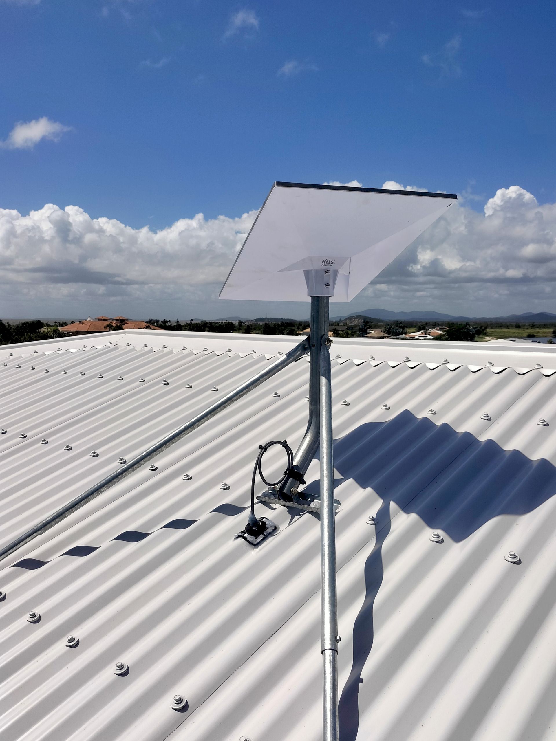 Solar panel mounted on a metal pole on a corrugated metal roof against a partly cloudy sky.