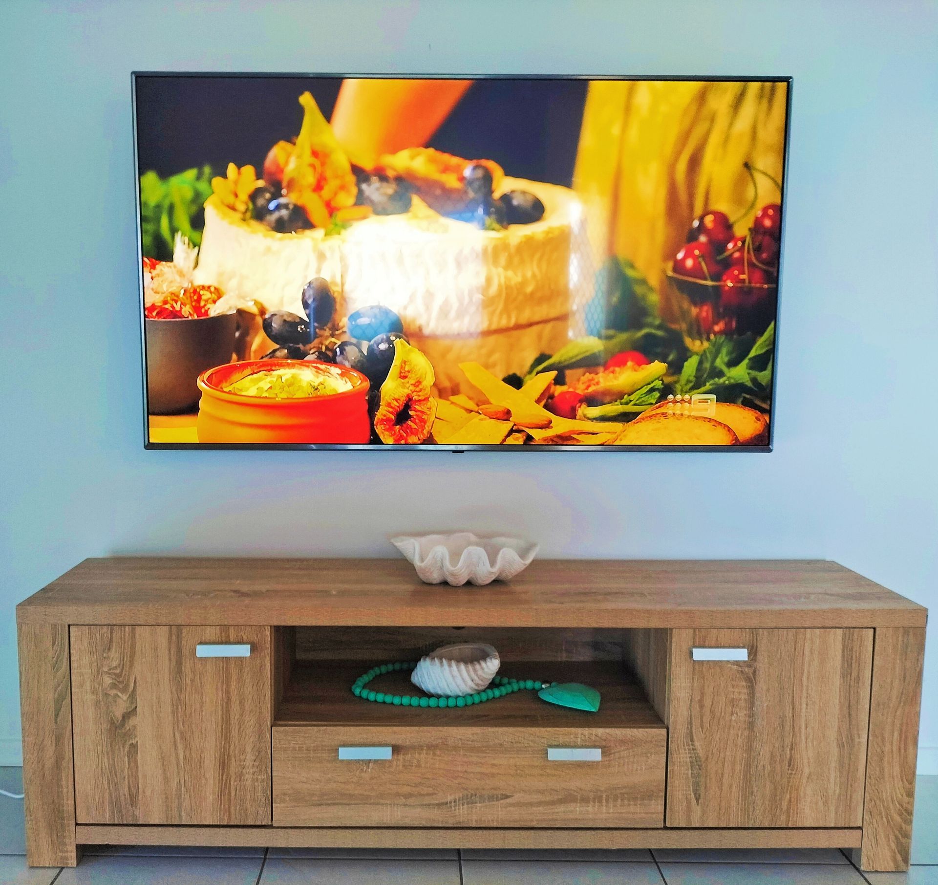 TV on a wall mount with tv playing and a brown cabinet underneath— Coastline Installations In Emu Park, QLD