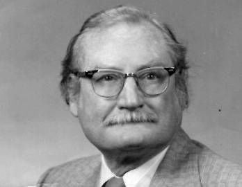 Harry V. Harlan with glasses and a mustache is wearing a suit and tie.