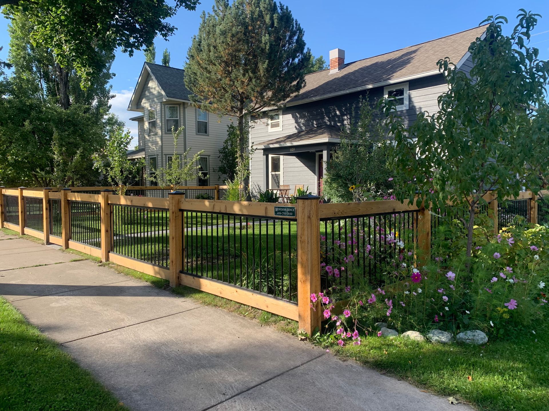 A wooden fence surrounds a lush green yard in front of a house.