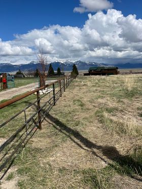 A fence surrounds a grassy field with mountains in the background.