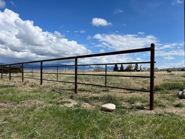 A metal fence surrounds a grassy field with mountains in the background.