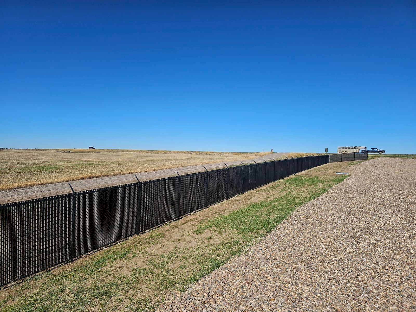 A fence along a gravel road in the middle of a field.