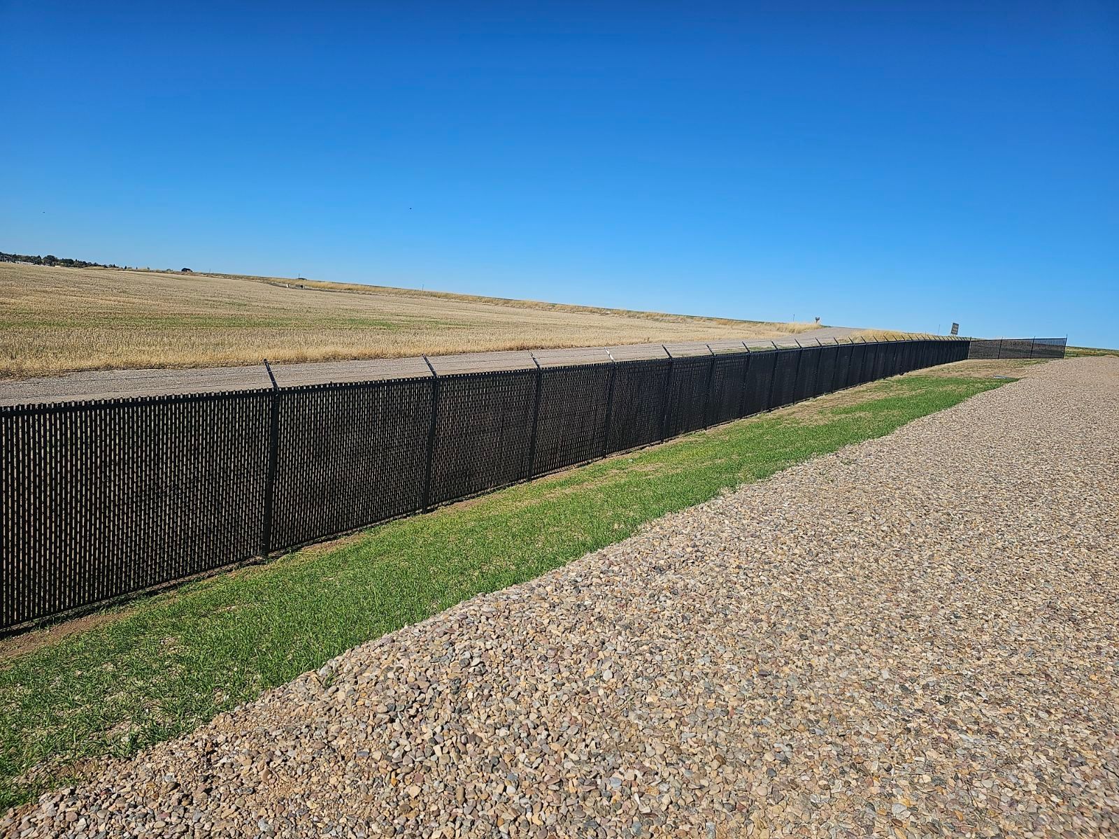 A long black chain link fence along a gravel road.