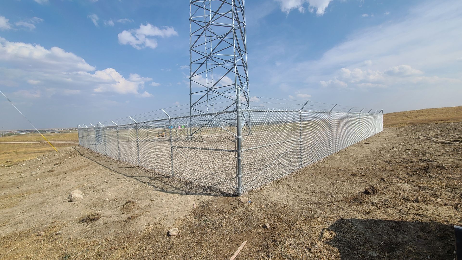 A barbed wire fence is surrounding a tower in a field.