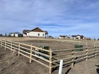 A wooden fence surrounds a dirt field with a house in the background.