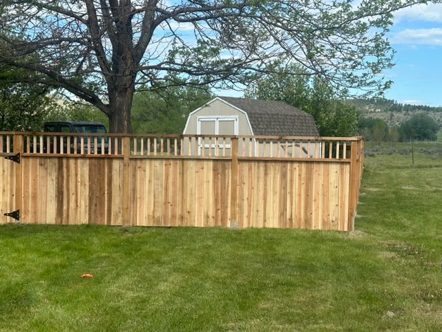 A wooden fence surrounds a yard with a barn in the background.